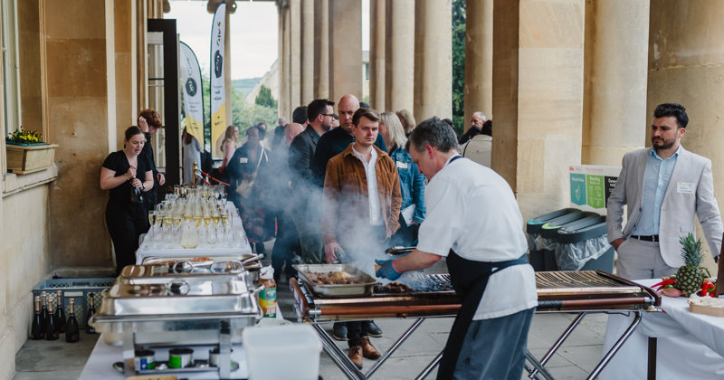 Chef cooking BBQ with table of drinks and guests in the background