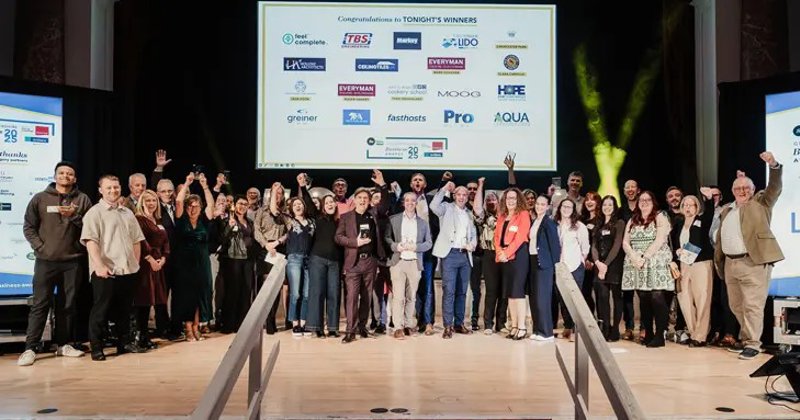 Group of people on stage with hands in the air and sponsors banner in the background