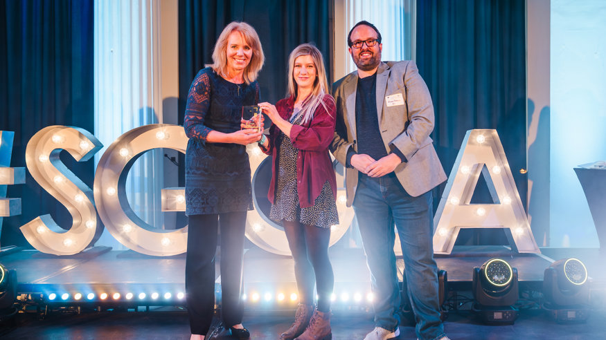Man with two ladies holding a trophy on a stage